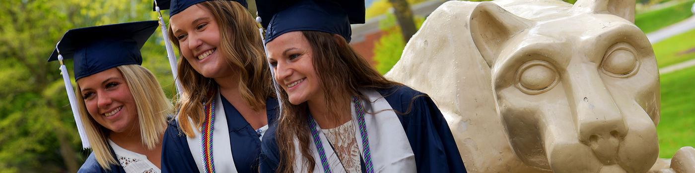 Three female graduates pose at the lion shrine on the Penn State 阿尔图纳 campus.